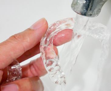 Patient rinsing clear aligner in sink