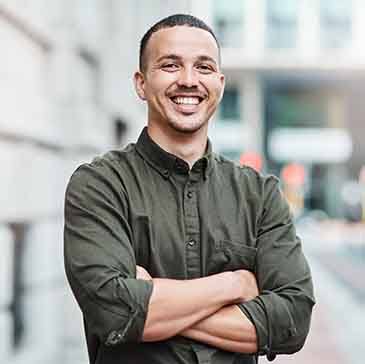 Man smiling with crossed arms outside building